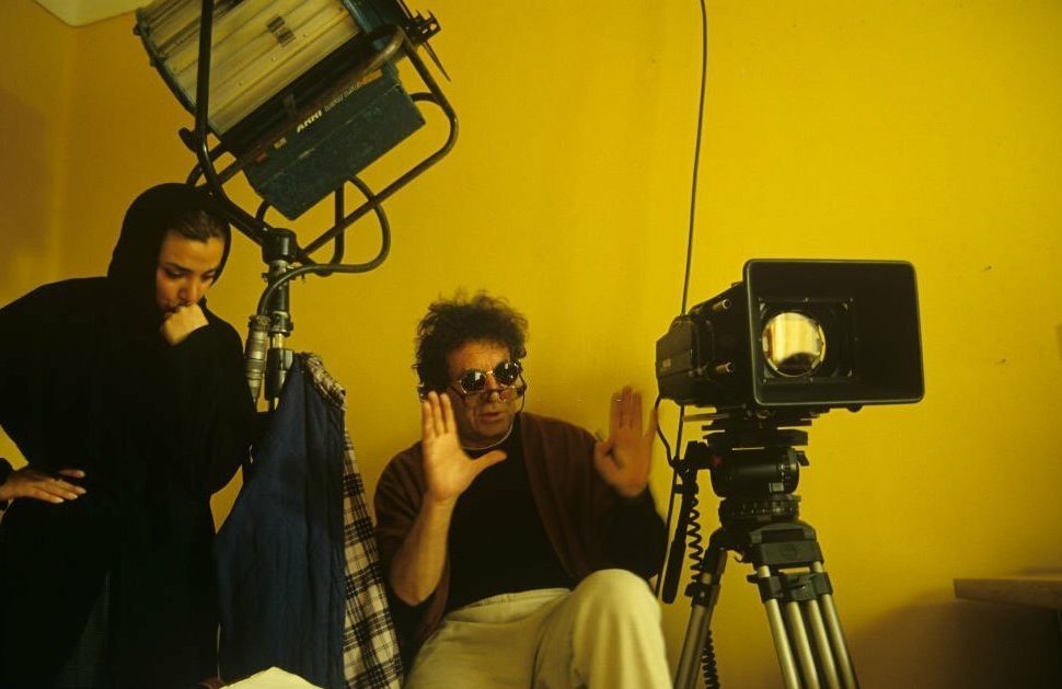 داریوش مهرجویی در پشتصحنهی فیلم درخت گلابی، عکس از کاوه کاظمی. dariush behrjui by kaveh kazemi Tehran, Iran, Dariush Mehrjui, famous Iranian director, during a break while directing "The Pear Tree", on location in Tehran, 1st February 1999. A veiled female assistant stands next to him. (Photo by Kaveh Kazemi/Getty Images)